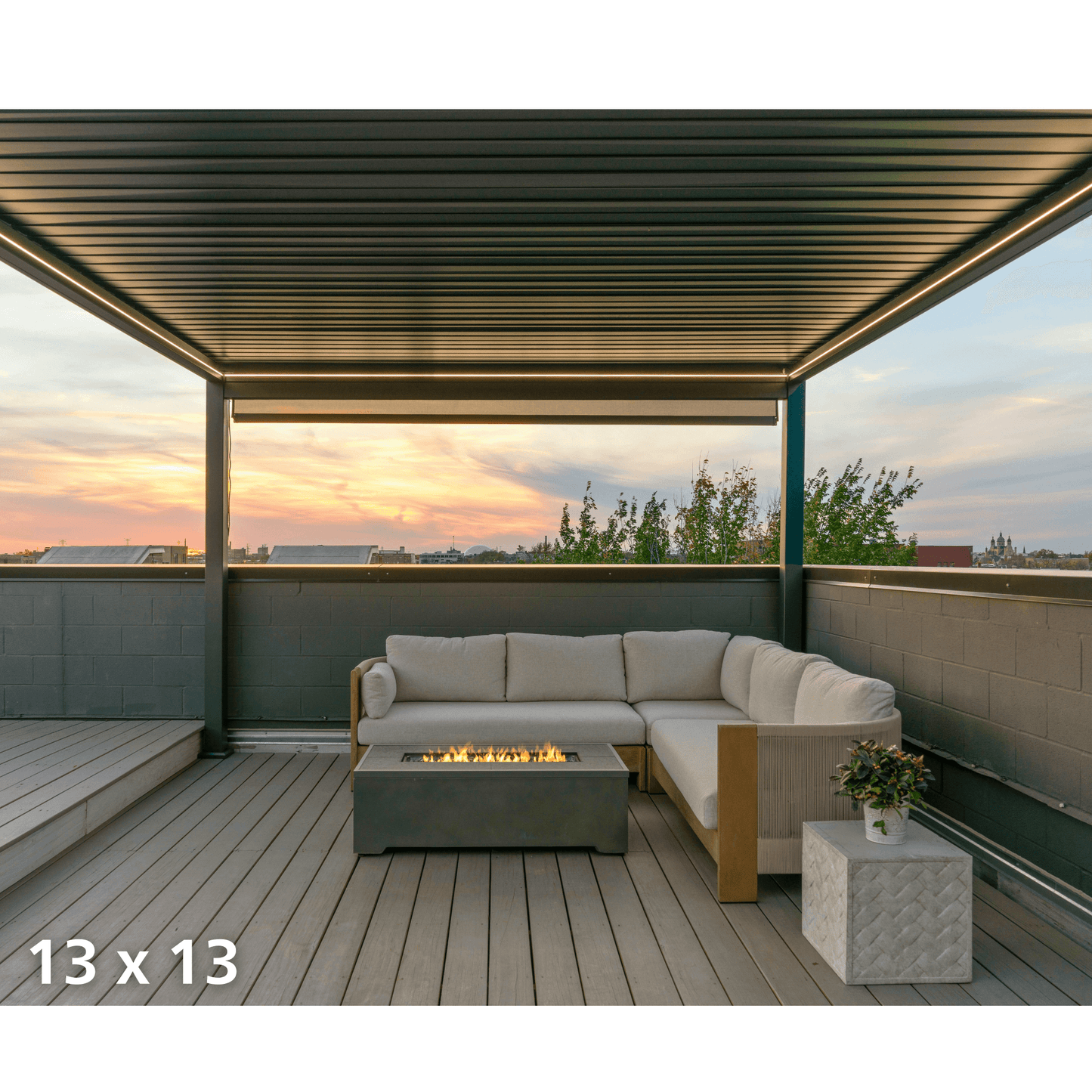 The Bon Pergola 13x13 rooftop lounge features partially open louvers, casting sleek shadow lines below. Its deep gray frame is accented with warm yellow LED strips along the edges, softly lighting the wood deck. Together with the gas firepit, the setup creates a cozy, romantic vibe at dusk.