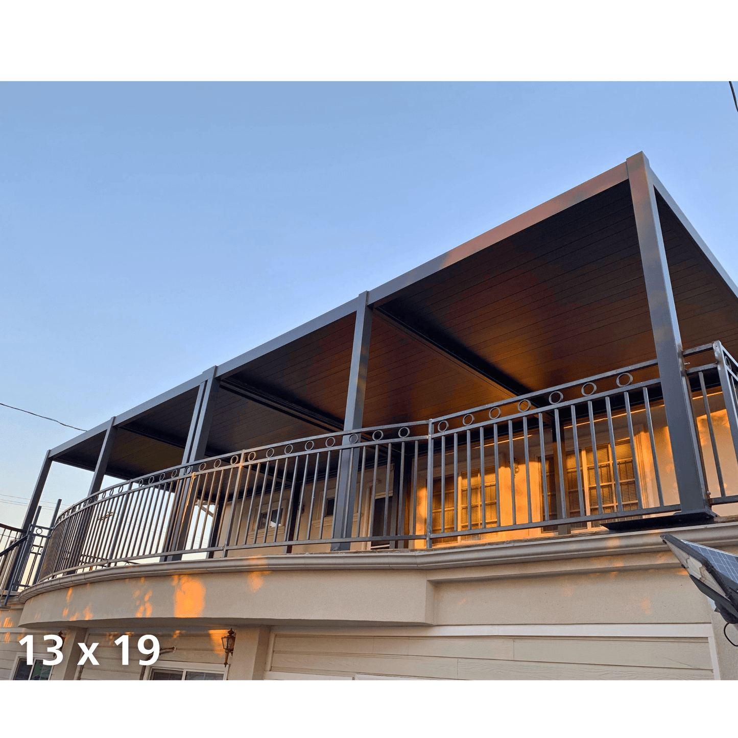 Two 13'x19' dark gray Bon Pergola motorized louvered roofs are installed side by side on a high-floor balcony. Both have closed louvers, creating a sleek, shaded canopy. The pergolas feature sturdy dark gray posts and beams, while the balcony below is enclosed by matching dark gray metal railings with circular and vertical bar detailing.