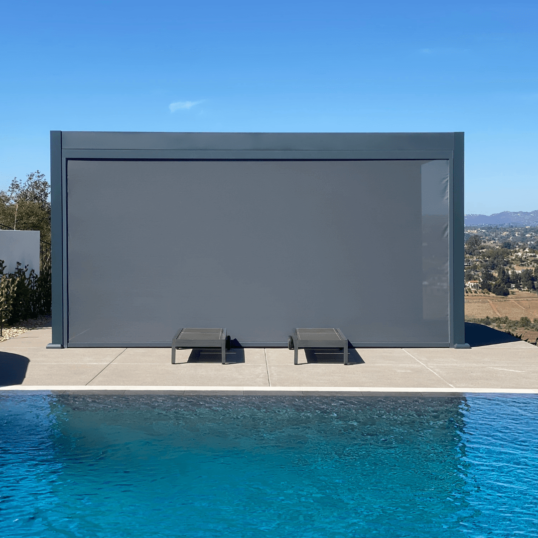 The gray Bon Pergola features a large dark gray windproof shade screen on its front, creating a semi-enclosed space facing the pool. The screen is nearly fully lowered, leaving just a small section open on the right side. Designed for wind, sun, and light water protection, the screen enhances comfort and privacy while helping block splashes from the pool, turning the pergola into a cozy outdoor retreat.