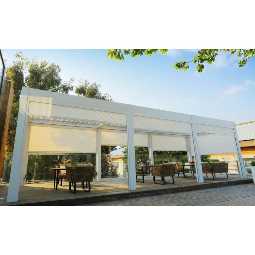 Several white Bon Pergolas are arranged side by side, creating a spacious outdoor dining area. Each pergola features white windproof shade screens on its sides. The terrace is covered with light-colored wooden flooring and furnished with multiple sets of outdoor dining tables and chairs, including dark metal tables and wicker chairs. Each table is set with tableware and decorations. The terrace is surrounded by lush green trees and plants, adding to the inviting, natural ambiance.