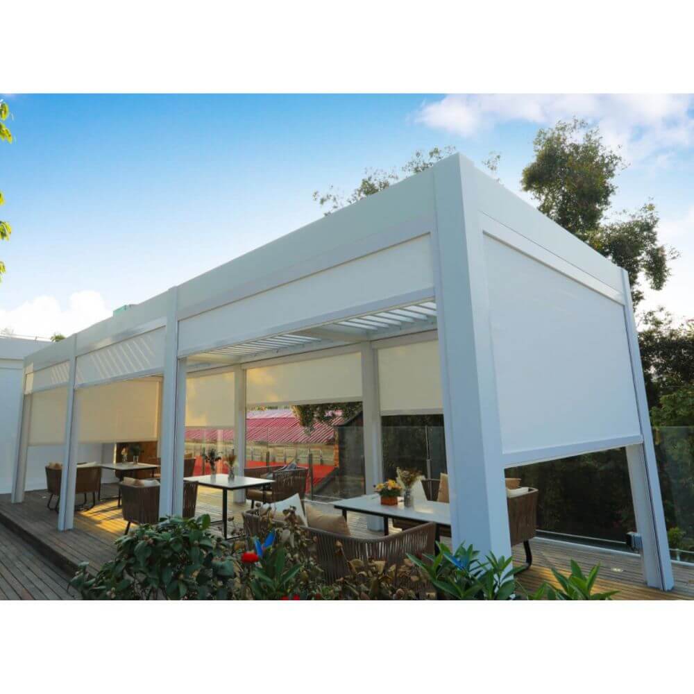 Three white Bon Pergolas are closely connected, each with a partially open white louvered roof. The sides feature white windproof shade screens, offering soft shade and privacy. Below, a terrace with dark brown wooden flooring is furnished with outdoor dining sets, including light metal tables and wicker chairs, each adorned with tableware and floral arrangements. The terrace is surrounded by lush greenery and trees, creating a peaceful and inviting outdoor space.