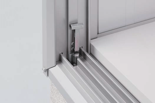 The sliding door track and roller assembly at the bottom of the Yodoko storage shed. You can see several parallel metal tracks, with some roller components embedded within and secured to the bottom of the door by metal brackets. There's also a small metal latch or fastening mechanism.