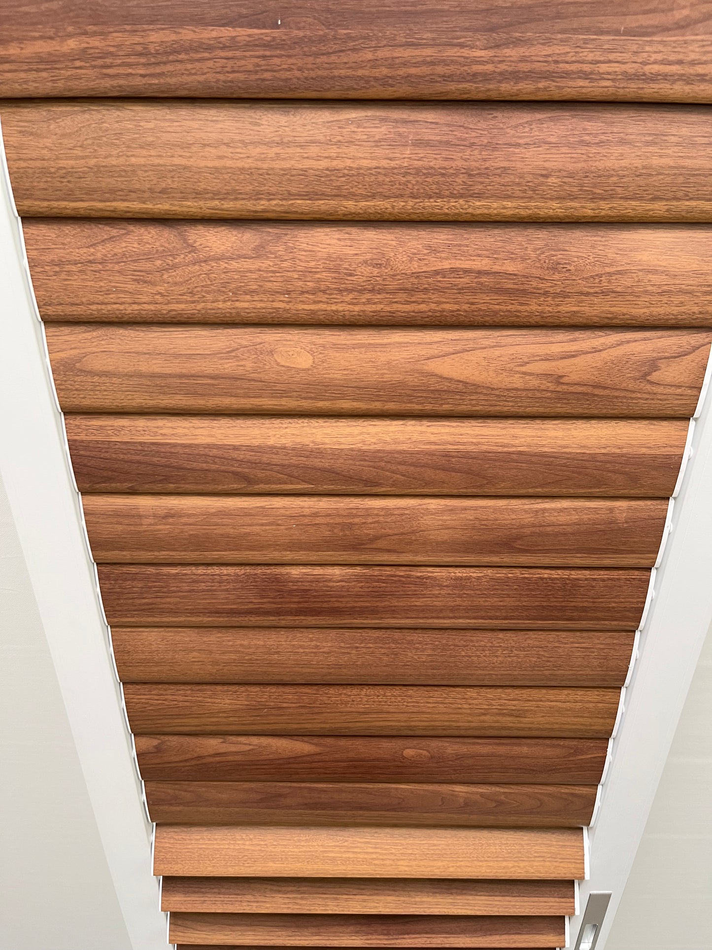 The faux wood presents a warm brown tone with clear, visible grain patterns. The planks, consistent in width, are arranged in parallel, creating a neat and layered visual effect. The white gaps may serve to enhance the sense of separation visually or act as structural connectors.