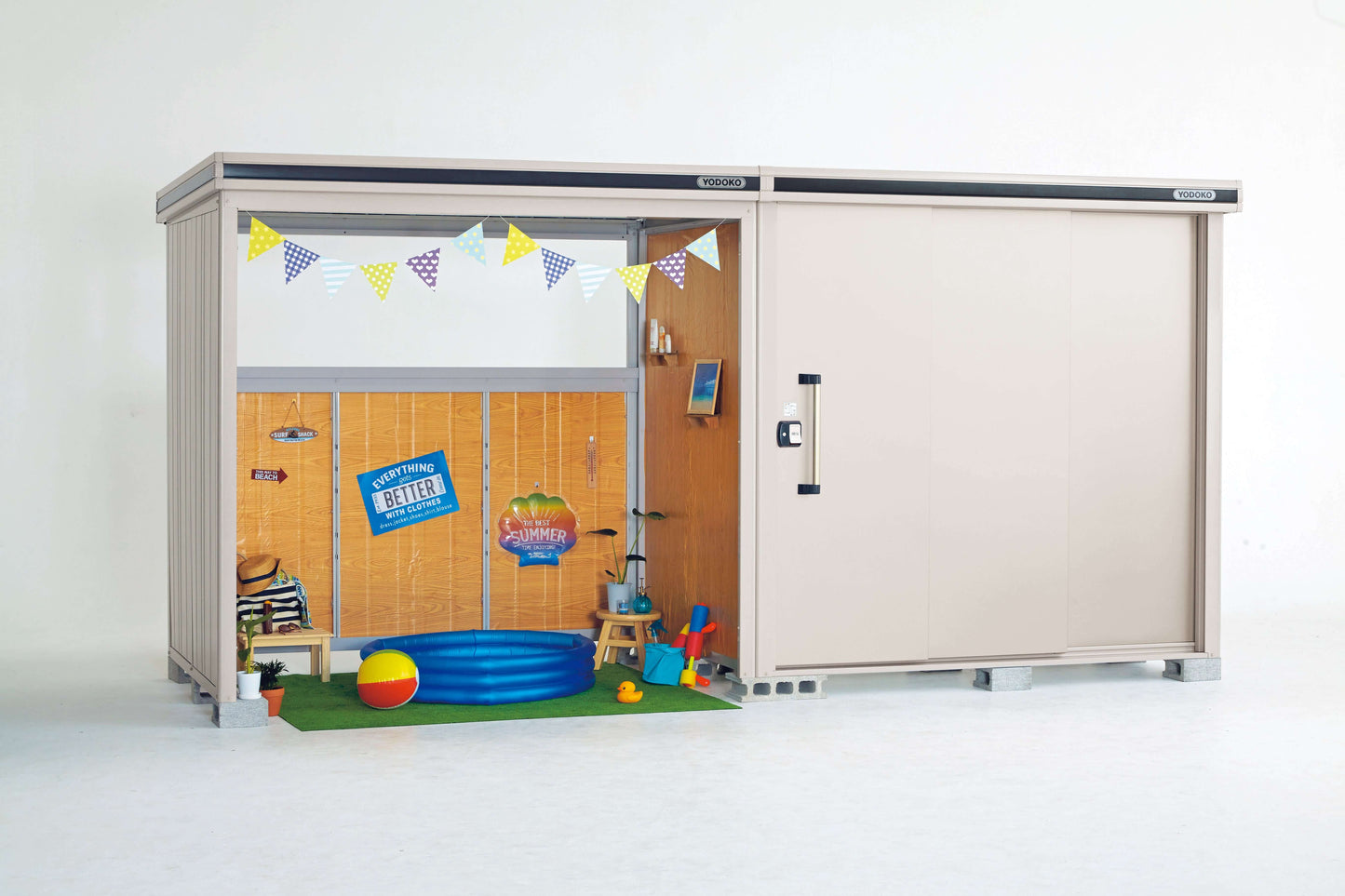 This is a product shot of the Yodoko ESF series light beige storage shed. One of the sliding doors is partially open, revealing a small space decorated with green artificial turf and summer-themed accents, including a blue inflatable pool, creating a fun and lively atmosphere. The other sliding door is closed, featuring a vertical black handle. The top and bottom edges of the shed have dark striped accents, giving it a metallic look. This design showcases its dual functionality as both a storage solution an