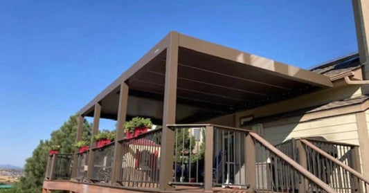 A bronze aluminum pergola with louvered roof panels installed on an elevated deck overlooking a coastal area.