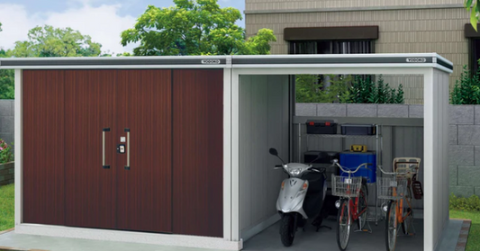 A gray steel metal shed with dark wood-style doors and an open storage bay on a lawn with a gravel pathway.