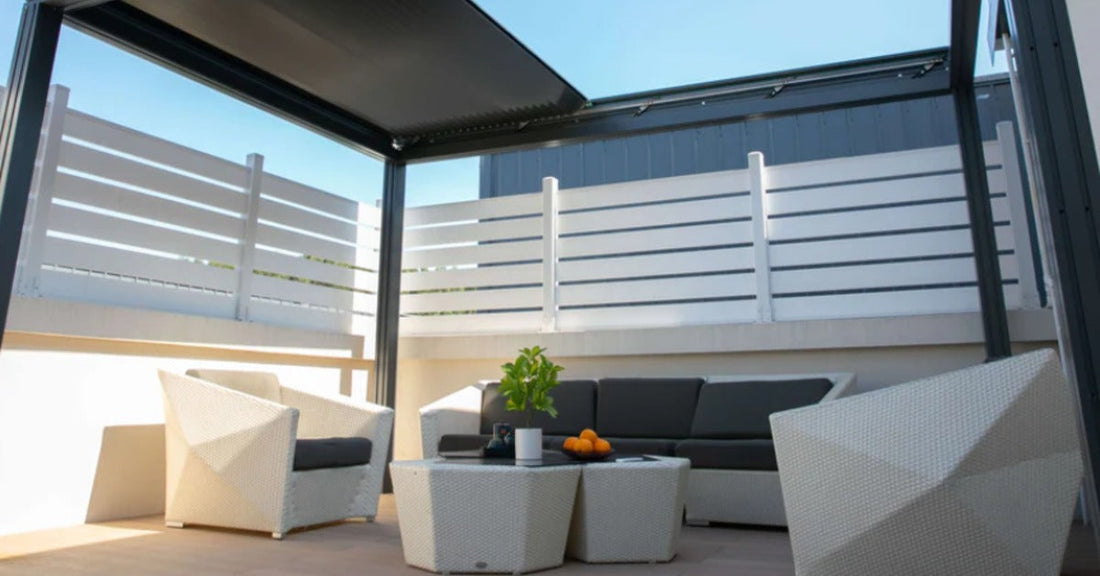 A black motorized pergola with retractable roof slats shading a rooftop patio with white wicker furniture.