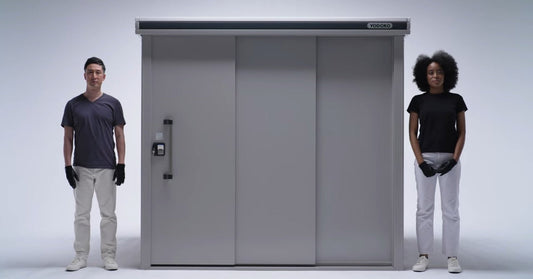A YODOKO steel metal shed with sliding doors shown next to two adults to illustrate its full size and scale.