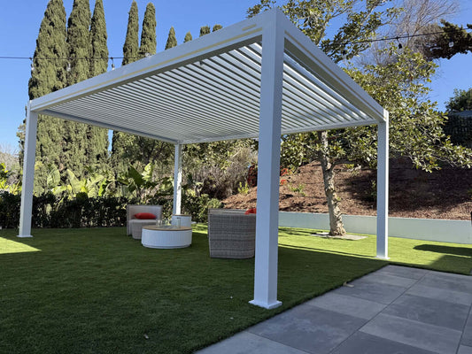 An outdoor living area with two couches and a round coffee table, under a paneled pergola surrounded by greenery.