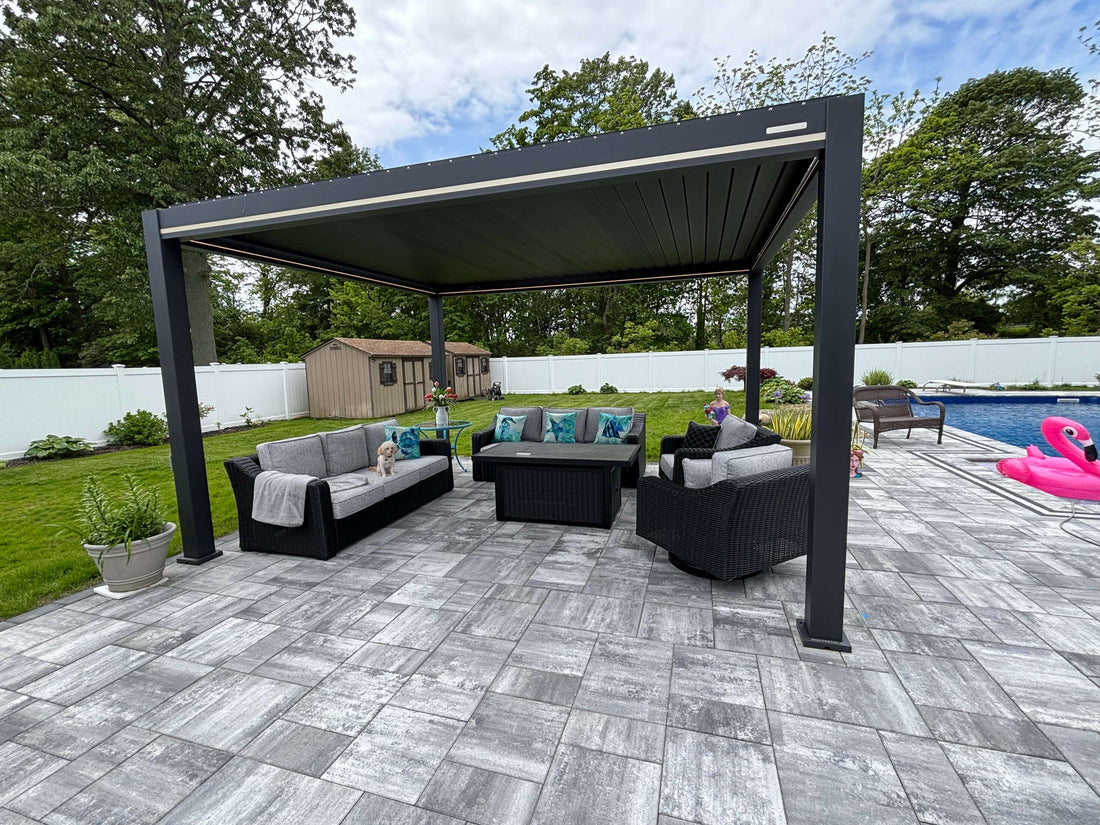 An aluminum pergola placed over a tiled floor over multiple long outdoor couches and a coffee table next to a pool.