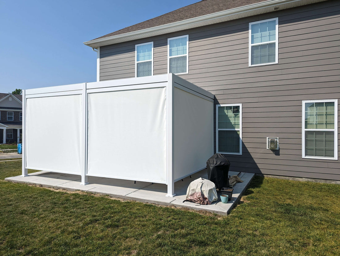 A large white, metal structure with plastic side covers placed on a concrete slab surrounded by grass in a backyard.