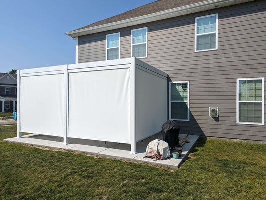 A large white, metal structure with plastic side covers placed on a concrete slab surrounded by grass in a backyard.