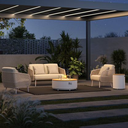 A deep gray Pergola with partially open louvers creates a cozy, modern outdoor space. Beneath the structure is an area with a deep gray outdoor rug, featuring a set of beige outdoor lounge furniture. The overall ambiance is warm, romantic, and contemporary. The deep gray pergola contrasts gently with the beige furniture, warm yellow lighting, and the glow of a fire, making it an ideal setting for relaxing, conversing, and enjoying outdoor time at night.
