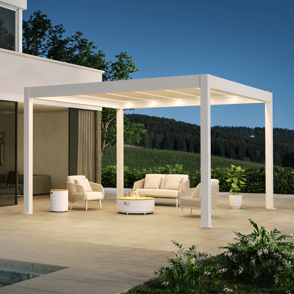 A white pergola with partially opened louvers features warm white LED strip lights integrated between the slats. The structure has a clean, modern design, built with thick white posts and beams. Below, a set of beige and light brown outdoor lounge furniture is arranged, including a two-seater sofa and two beige woven armchairs, all with matching beige cushions. At the center of the seating area sits a white round coffee table, topped with a gas fire pit enclosed by a clear glass wind guard.