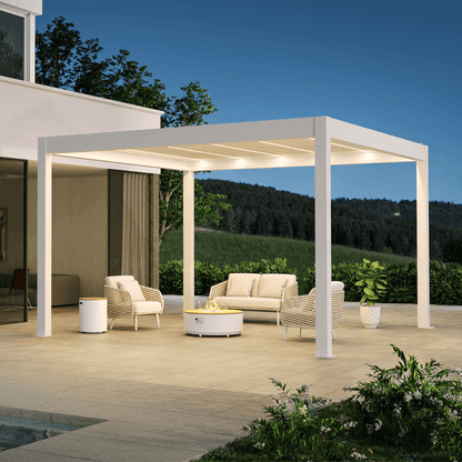A white pergola with partially opened louvers features warm white LED strip lights integrated between the slats. The structure has a clean, modern design, built with thick white posts and beams. Below, a set of beige and light brown outdoor lounge furniture is arranged, including a two-seater sofa and two beige woven armchairs, all with matching beige cushions. At the center of the seating area sits a white round coffee table, topped with a gas fire pit enclosed by a clear glass wind guard.