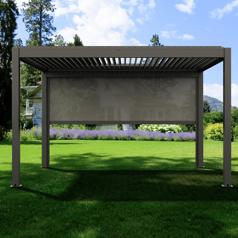 A dark gray Bon Pergola with motorized louvers is showcased during the day, with the louvers partially open, casting sleek, linear shadows below. One side of the pergola features a matching dark gray sunshade screen. The overall vibe is fresh, serene, and naturally inviting. The deep gray structure blends harmoniously with the surrounding greenery and the backdrop of blue skies and fluffy white clouds.