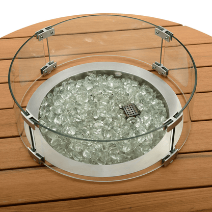 The central burner and surrounding details of the Cypress Collection Fire Pit showcase a square metal burner with small circular holes across the top, designed to emit flames. The area around the burner is filled with transparent glass pebbles of varying sizes, their smooth surfaces reflecting light with a crystalline shine. Encircling the pebbles is a round transparent glass wind guard. The tabletop is made of parallel wood slats, with subtle gaps between them, mimicking the texture of natural wood.