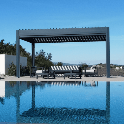 A dark gray Bon Pergola with a motorized louvered roof sits on a light gray platform, positioned next to a clear blue swimming pool. The louvers are partially open, allowing sunlight to filter through the deep gray slats, creating a bright and inviting outdoor space.