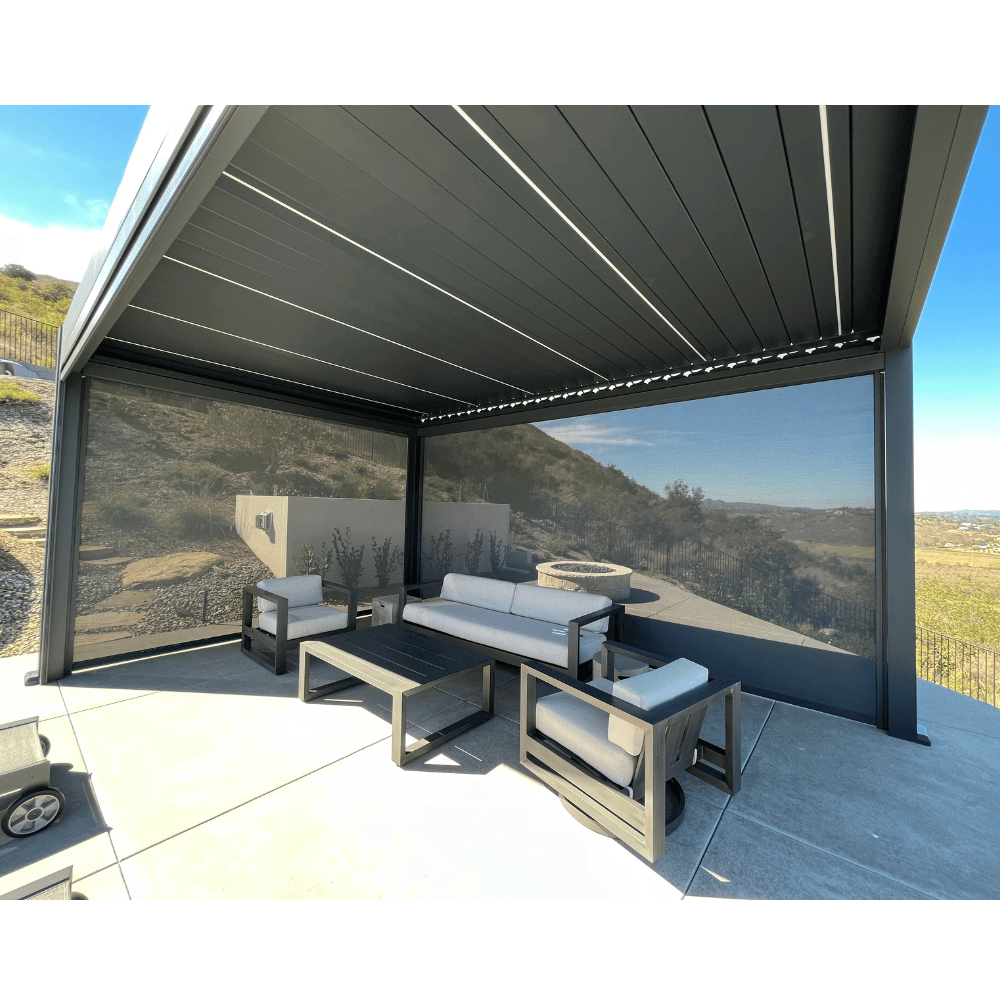 The dark gray Bon Pergola features a motorized louvered roof with dark shade screens on two sides for added privacy and weather protection. It sits on a light gray-floored platform, furnished with modern outdoor pieces—including a light gray sofa, two gray armchairs, and a dark gray coffee table—creating a stylish and comfortable lounge area.