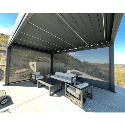 The dark gray Bon Pergola features a motorized louvered roof with dark shade screens on two sides for added privacy and weather protection. It sits on a light gray-floored platform, furnished with modern outdoor pieces—including a light gray sofa, two gray armchairs, and a dark gray coffee table—creating a stylish and comfortable lounge area.