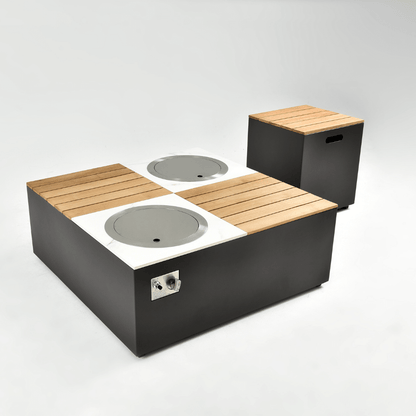 The square gas fire pit coffee table features a dark gray base with a tabletop divided into four sections. A round gas burner is inset at each diagonal, and when not in use, the circular glass wind guard can be replaced with a metal round cover. The side of the coffee table is equipped with a metal control panel, which includes knobs and an ignition system.
