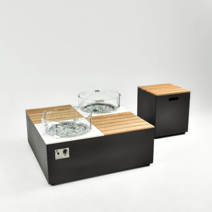 The square gas fire pit coffee table features a dark gray base, divided into four sections, with a round gas burner inset at each diagonal. The burners are surrounded by decorative stones and encased in a transparent round glass wind guard. The side of the coffee table includes a metal control panel, complete with knobs and an ignition system. The storage box is made from the same material as the coffee table base, with a light-colored faux wood slat top and rectangular handle openings on the sides.