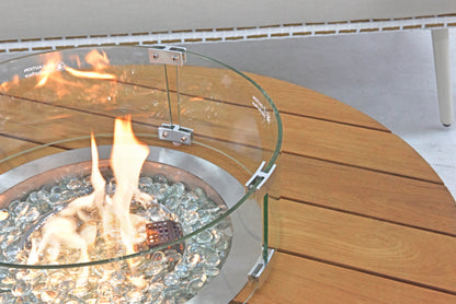 The outdoor gas fire pit is positioned on a wooden tabletop, surrounded by a curved transparent glass wind guard that combines both functionality and aesthetic appeal.