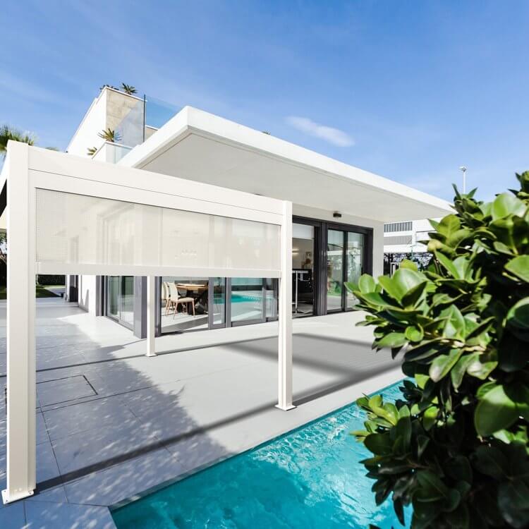 A modern white Bon Pergola is set by a swimming pool, featuring a sleek structure with slender white posts and beams. One side has a partially lowered manual retractable shade screen for extra sun protection and privacy. The platform is next to a clear blue pool, creating a serene atmosphere. The pergola blends seamlessly with the light gray flooring, blue pool, and white residence, offering a stylish, resort-like outdoor space that's perfect for relaxation and comfort.