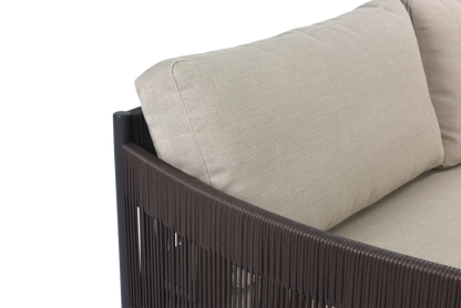 A detailed close-up of a modern outdoor sofa corner. The thick seat and back cushions are upholstered in light beige, linen-textured fabric. The sofa boasts a bold black metal frame, while the side panel features tightly woven vertical dark brown lines, adding rich texture and a sleek, uniform look to the design.