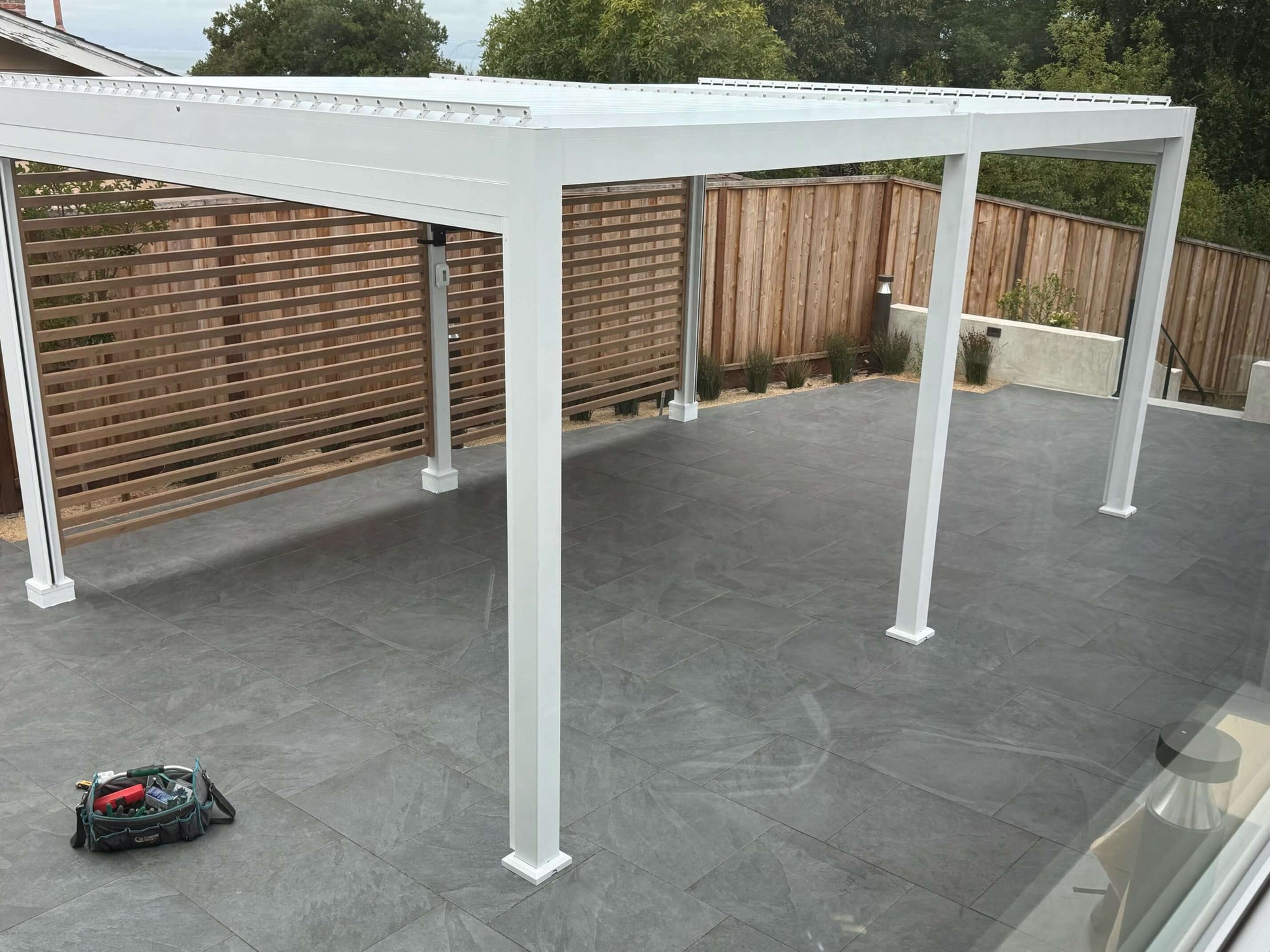 White 6 posts louvered pergola with wood grain slat fencing on a modern slab patio 
