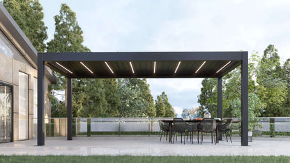 A dark gray Bon Pergola with a motorized louvered roof and integrated LED lighting sits on a light gray paved patio, surrounded by tall green trees. The louvers are partially open, revealing deep gray slats with built-in white LED strips that remain visible even in daylight. The pergola’s clean, modern design features sturdy dark gray beams and posts, creating a sleek and stylish outdoor space.
